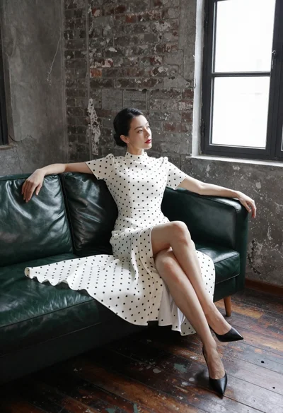 Woman in white polka dot dress seated on green leather sofa