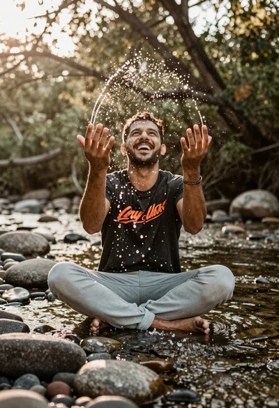 Man sitting cross legged splashing water in shallow river stream bed
