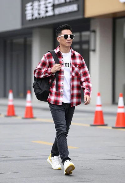 Man walking down urban street wearing plaid shirt and jeans