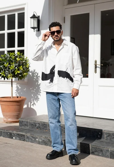 Stylish man in white shirt and jeans standing outdoors near white building
