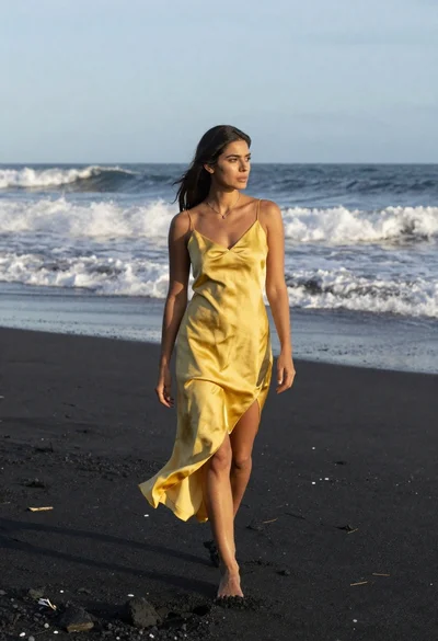 Woman in yellow slip dress walking on black sand beach near ocean