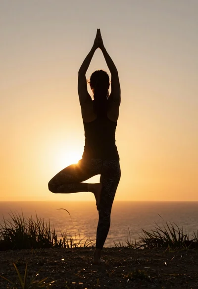 Silhouette of woman practicing yoga tree pose against glowing ocean sunset