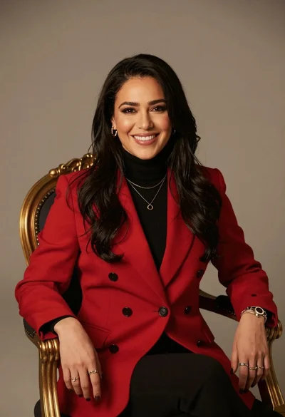 Smiling woman in red blazer seated on ornate gold chair against neutral