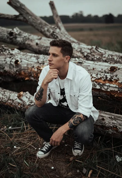 Man crouching contemplatively among large fallen tree trunks outdoors