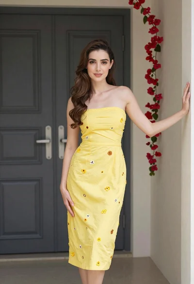 Young woman in yellow embroidered dress standing indoors near red flowers