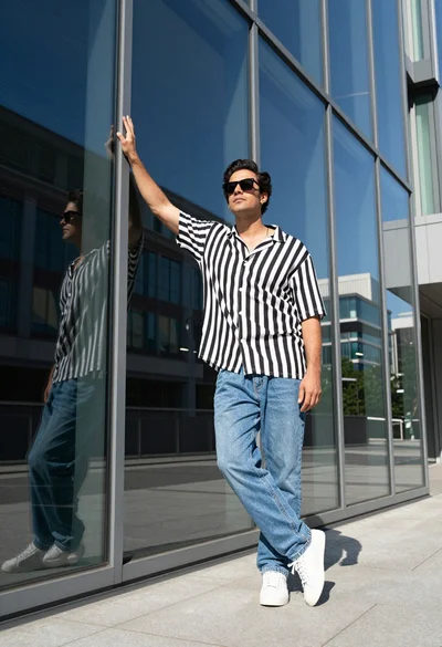 Stylish man in striped shirt posing against modern glass building facade