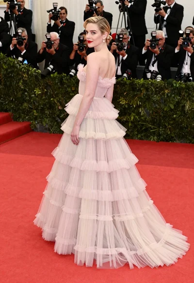 Blonde woman in pink tulle gown on red carpet looking back