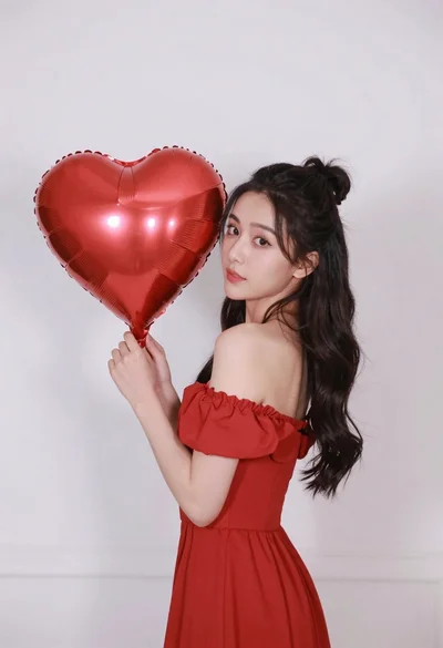 Woman in red dress holding heart shaped balloon against white wall