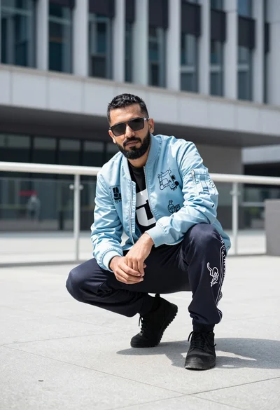 Man crouching in urban plaza wearing bomber jacket looking at camera