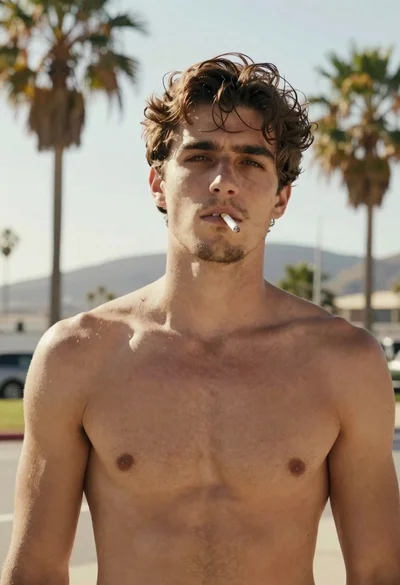 Shirtless young man with brown hair standing before palm trees at sunset