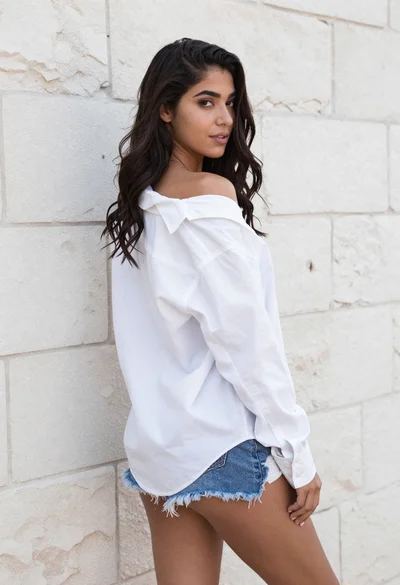 Young woman in white shirt and denim shorts against textured stone wall