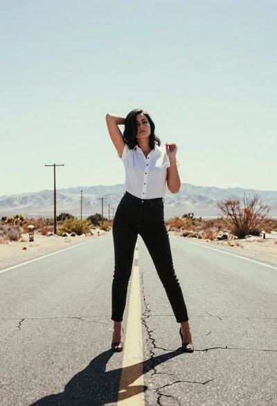 Woman in white shirt and black jeans on desert highway under mountains
