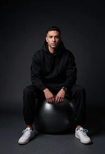 Man sitting on black exercise ball in dark studio