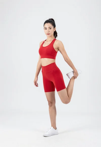 Fit woman in red athletic wear stretching on white studio background