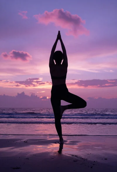 Silhouette of person practicing yoga in tree pose on wet beach at