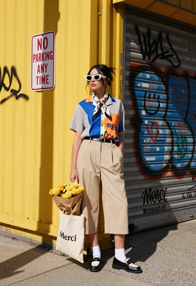 Stylish woman in graphic shirt and culottes stands on urban street corner