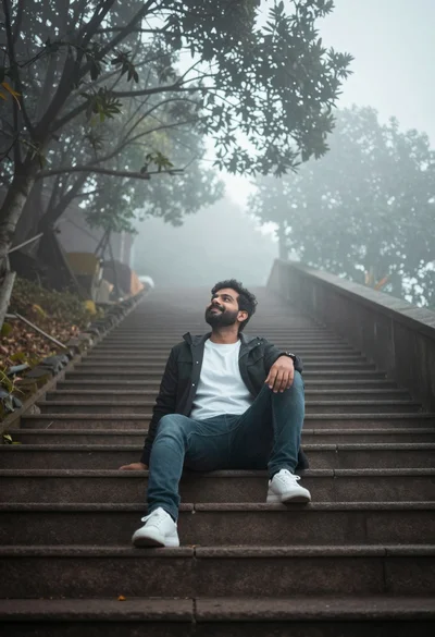 Man sitting on wide stone staircase in misty outdoor setting looking up