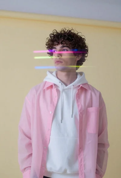 Young man in sheer pink shirt against pale yellow wall with light