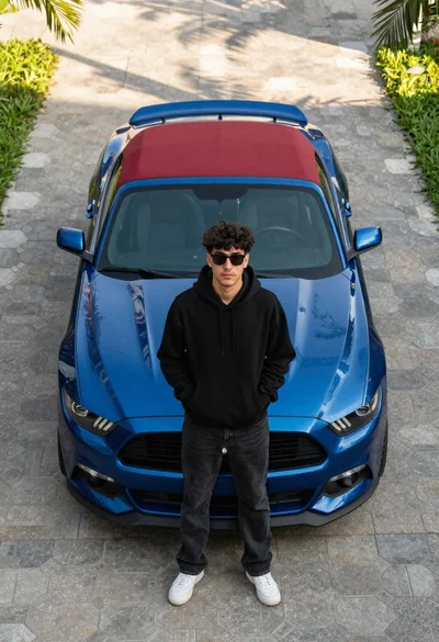 Young man standing by blue convertible sports car on paved driveway