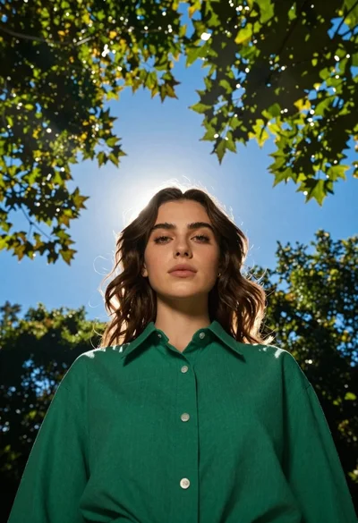 Young woman in green shirt standing under trees against blue sky
