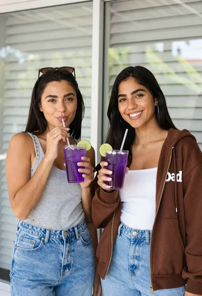 Two smiling women holding purple drinks in front of glass windows