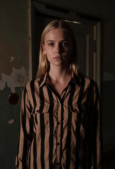 Fair skinned woman with straight blonde hair in striped shirt inside dimly