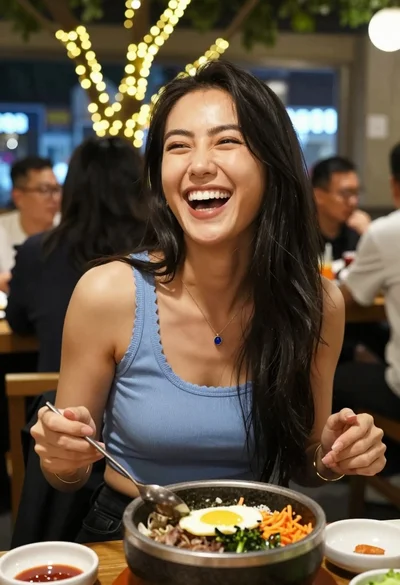 Joyful woman laughing at restaurant table with bibimbap in foreground
