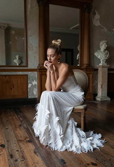 Blonde woman in white feather gown sitting in rustic high ceiling room