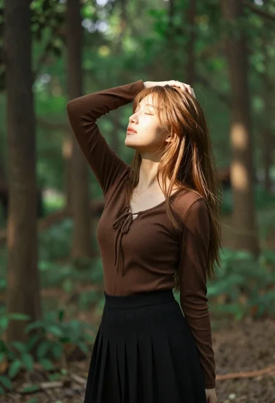 Young woman in brown top standing in sun dappled forest