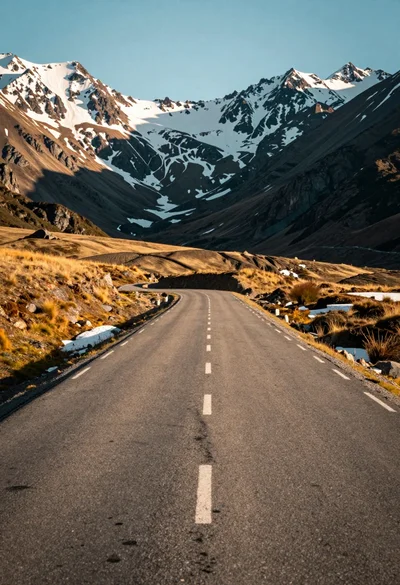 Winding asphalt road through rugged terrain beneath towering snow capped mountains
