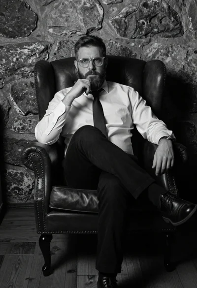 Low angle cinematic portrait of bearded man in armchair against stone wall