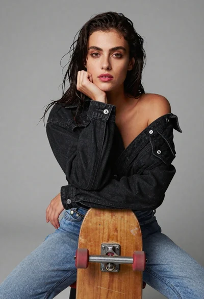 Young woman sitting with skateboard against gray background