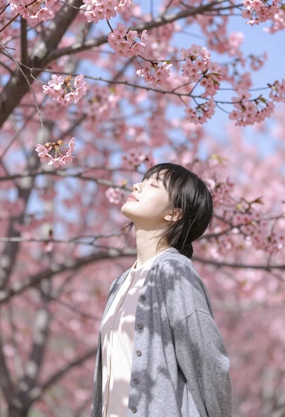 Young woman with dark hair standing under pink cherry blossom canopy