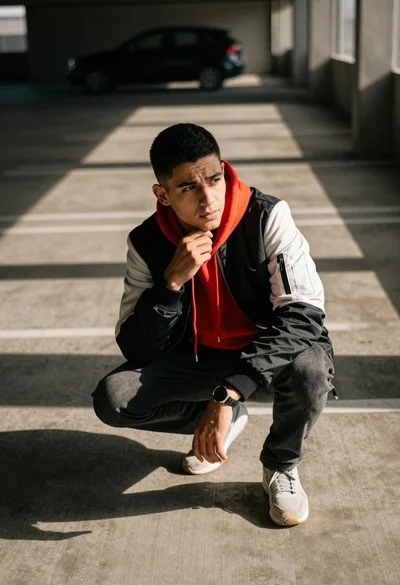 Man crouching in dimly lit parking garage with strong sunlight casting long