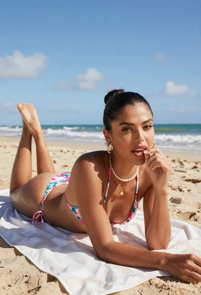 Fit woman in floral bikini lying on beach towel under bright blue