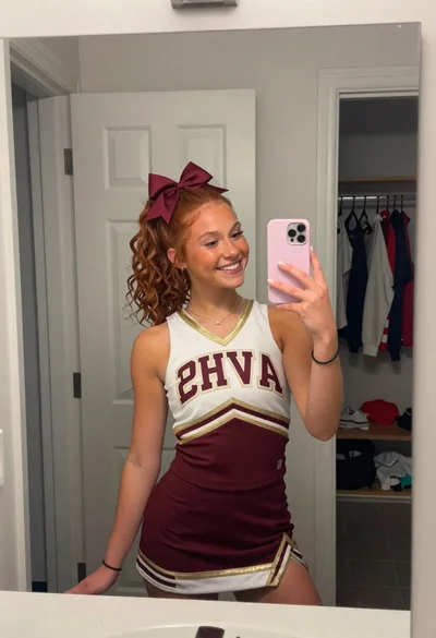 Young woman in cheerleading uniform taking a mirror selfie indoors