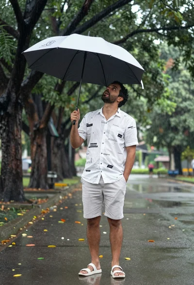 Man under black and white umbrella standing on paved road surrounded by