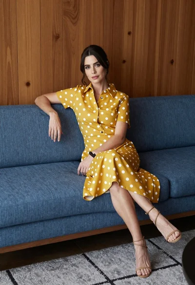 Woman in polka dot midi dress seated on blue sofa indoors