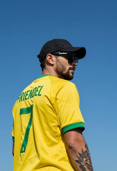 Man in yellow soccer jersey standing against clear blue sky background