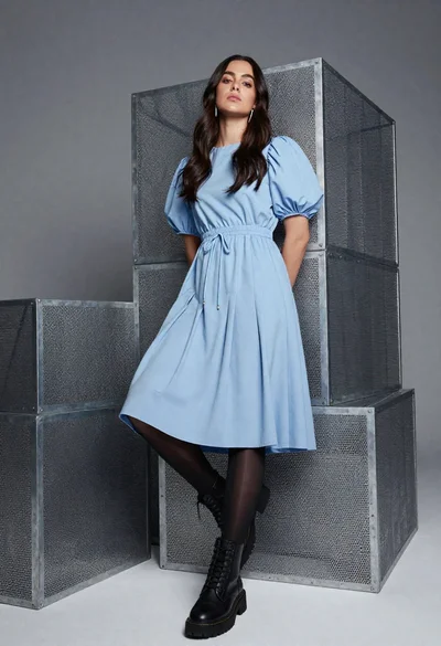 Young woman in blue midi dress leaning against metal cubes studio setting