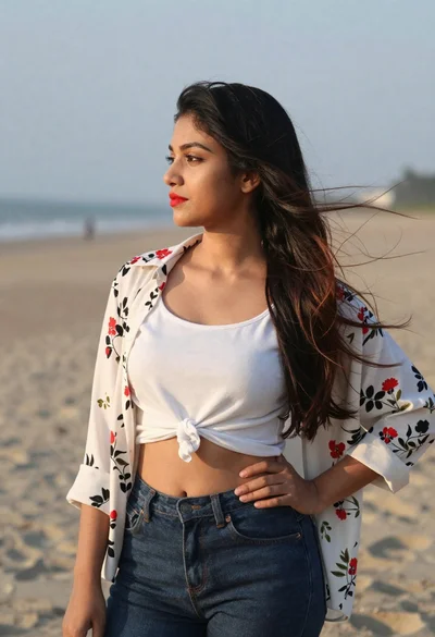 Young woman in white top and jeans standing on sandy beach