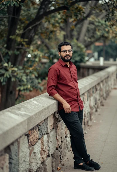 Man leaning against stone wall outdoors with blurred foliage background