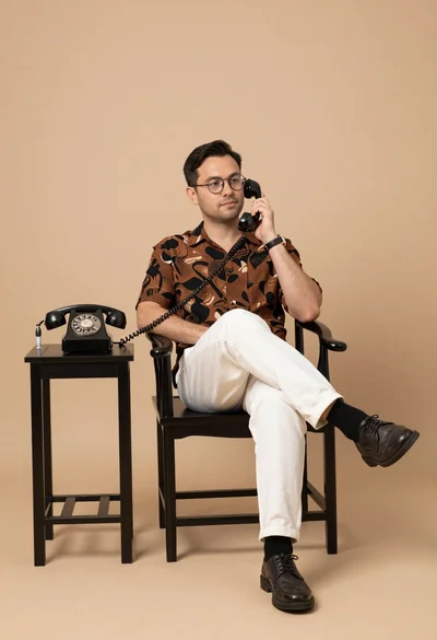Man in patterned shirt sitting casually with vintage telephone receiver in studio