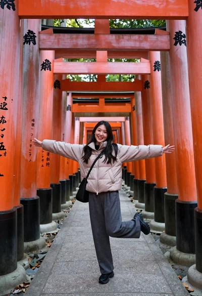 Young woman in puffer jacket posing inside a tunnel of orange torii