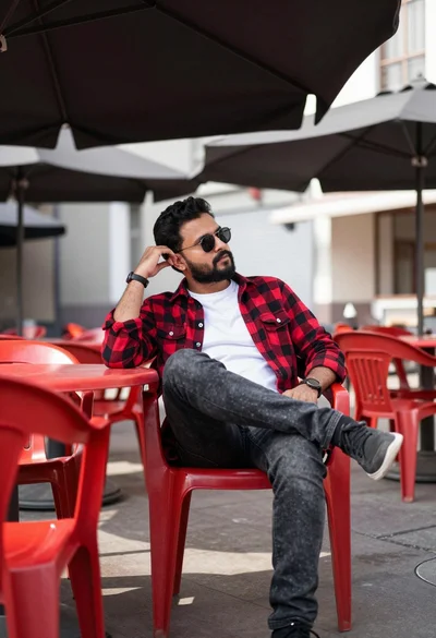 Man sitting casually at outdoor cafe under large umbrellas with red furniture