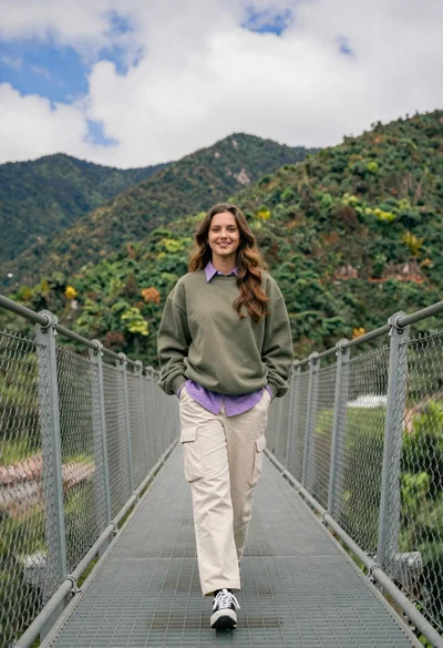Young woman in olive sweatshirt walking on metal bridge with mountains