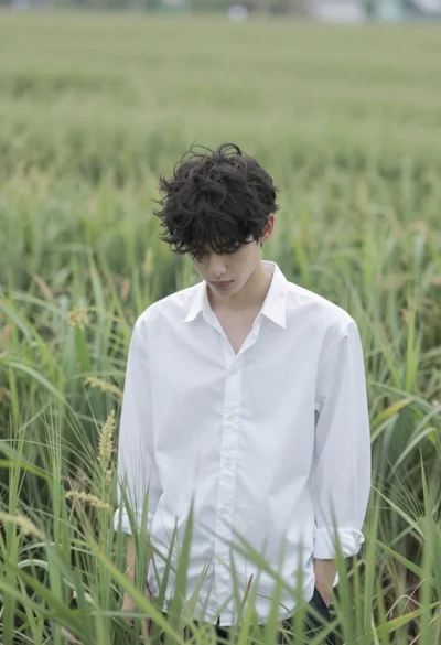 Young man in white shirt standing in tall swaying green grass field