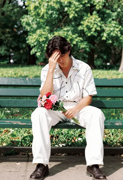 Man sitting on park bench holding flowers in pensive pose outdoors