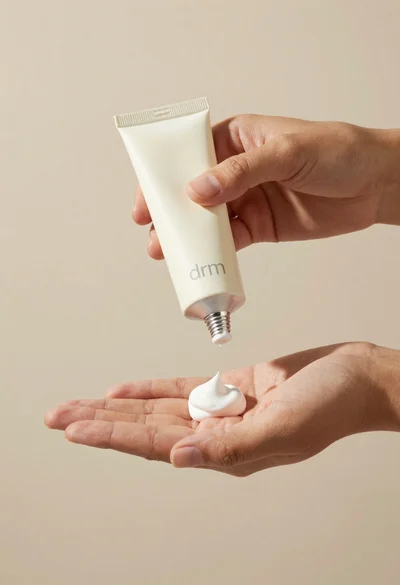 Hands dispensing white cream from a tube into a palm