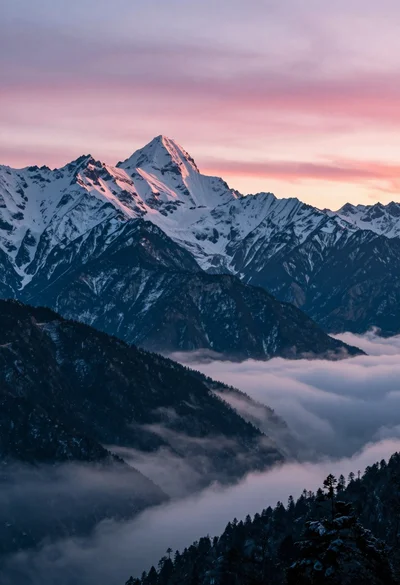 Majestic snow capped mountain range above sea of clouds at twilight